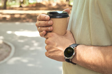 Craft paper cup with coffee in the hand of a man with a clock. Disposable paper cup close up. A man...