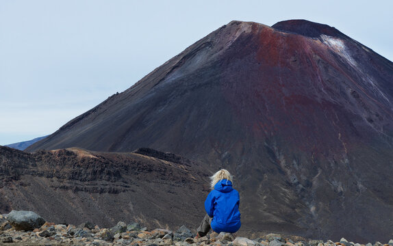 Rear view of a woman sitting on a rock looking at volcano, Tongariro National Park, North Island, New Zealand