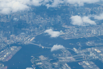 Aerial view of Tokyo bay near Odaiba with a rainbow bridge from an airplane on sunny day. Looking down and flying over the clouds and and industrial zone (Kawasaki - Tokyo), Japan. 