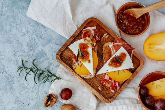 Overhead view of two slices of toast with serrano ham, cheese, persimmon and chutney