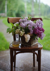 A bouquet of lilacs in a basket on a chair in the rain.