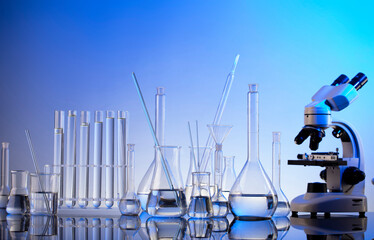 Laboratory investigations. Microscope, glass tubes and beakers on blue background.
