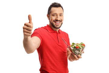 Smiling young man in a red t-shirt eating a healthy fresh salad and showing thumbs up