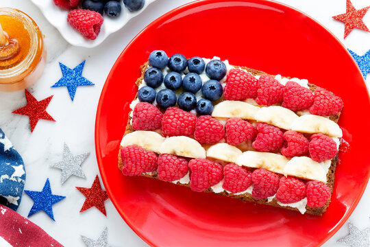 American flag sandwich with fresh fruit like raspberries, banana and blueberries on rye bread with patriotic decoration for Independance Day celebration