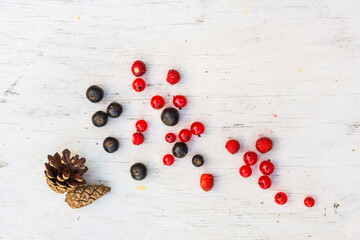 Berries red and black currants with strawberry and pine cones are scattered on the old wooden table