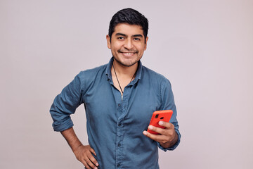 Hombre joven y feliz con un celular. Modelo aislado en fondo blanco con camisa azul
