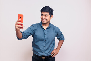 Hombre joven y feliz tomando una foto selfie mientras sonrie. Modelo aislado en fondo blanco camisa azul