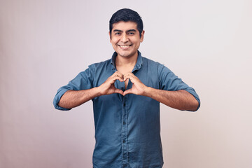 Hombre joven y feliz hace gestos de amor con sus manos. Modelo aislado en fondo blanco con camisa azul