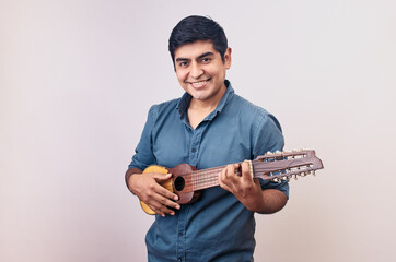 Hombre joven y feliz sonriendo en primer plano con un charango. Modelo aislado en fondo blanco con...