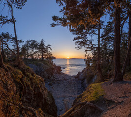 Obraz na płótnie Canvas A sunset over the ocean viewed for a forested cove with tress on both sides of the image from Anacortes Island.