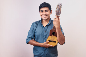 Hombre joven y feliz sonriendo en primer plano con un charango. Modelo aislado en fondo blanco con...