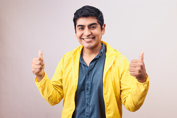 Hombre joven y feliz levanta pulgares. Modelo aislado en fondo blanco con casaca amarilla