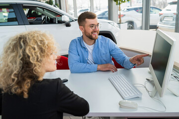 Car dealership manager with client at computer in showroom