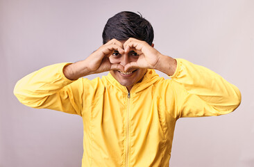 Hombre joven y feliz hace gestos de amor con sus manos. Modelo aislado en fondo blanco con casaca amarilla