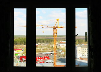 In the window-a construction crane. Construction site under the window in the summer . Construction crane on the blue sky in the window.