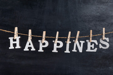 Word HAPPINES held on a clothespin on a rope against black background. Inscription from white...