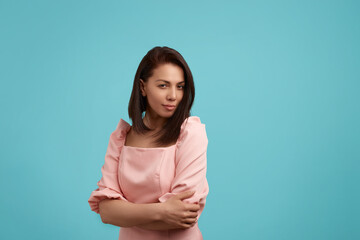 Obraz premium Playful coquettish caucasian female in pink dress, smiling shyly at camera as if flirting. Having joyful expression on her face, isolated over blue background. People expression concept.