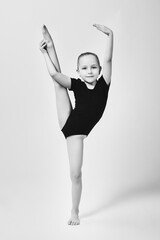 little gymnast demonstrates flexibility and balance in a gymnastic pose by lifting her leg