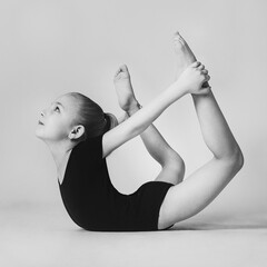 a little girl stands in a gymnastic pose, bending over her stomach and holding her legs