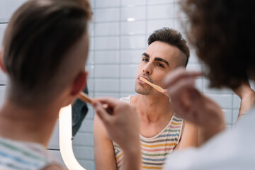 Gay couple cleaning his teeth with a sustainable bamboo toothbrush, in the bathroom in the morning...