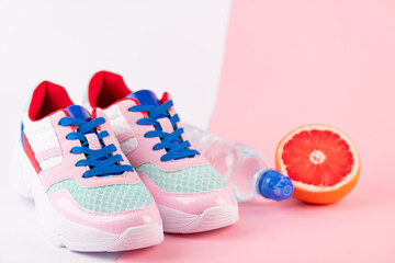 Fototapeta na wymiar Sport equipment sport shoes, bottle of water, citrus fruits on pink and white background. Healthy lifestyle, fitness, diet, slimming concept. Trendy female sport accessories, copy space