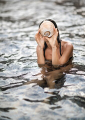 Female in water holding sea shell in front of her face. Summer vacation and relaxation concept.