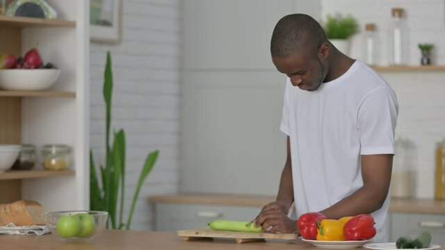 Healthy African Man Cutting Cucumber in Kitchen 