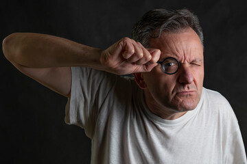 A man holds a magnifying glass in front of one eye looking through it with a very funny expression