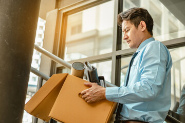 Businessman is carrying a brown cardboard box to resignation - obrazy, fototapety, plakaty