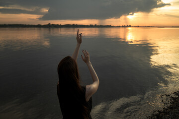 girl tries to touch the rays of the setting sun, arms outstretched towards the setting suт
