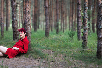 Young woman in red dress posing in pine forest