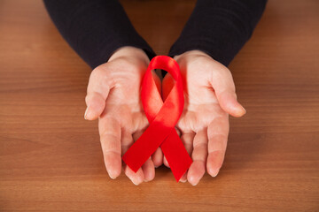 Red ribbon - symbol of awareness and support for those living with HIV, wooden background, woman's...