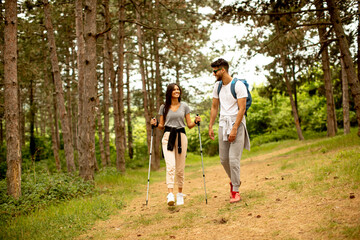 Fototapeta premium Smiling young couple walking with backpacks in the forest