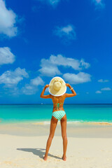 Obraz premium Girl in bikini having fun at the beach, standing on the beach with beach hat, looking at horizon, interracial, black