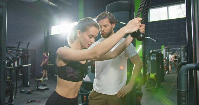 Trainer support. Athlete woman doing push ups with trx fitness straps in the gym while join lessons in sport club under the supervision of a coach. Workout and healthy lifestyle concept