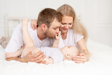 Obraz na płótnie Canvas happy family mom, dad and baby play on the bed at home and have fun