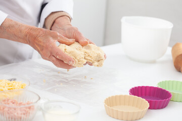 Senior woman preparing dough for a delicious cheese and ham tartlet