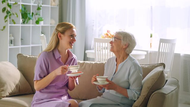 Young daughter and elderly mom with cups of tea at home