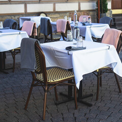 View of empty street cafe restaurant outdoor terrace veranda decoration on pedestrian european street, with chairs, tables decorated with white tablecoth, pink and grey blanket, bottles of water