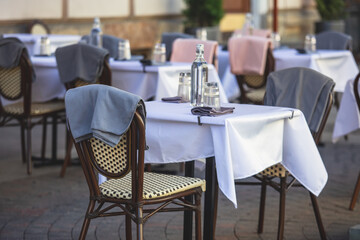 View of empty street cafe restaurant outdoor terrace veranda decoration on pedestrian european street, with chairs, tables decorated with white tablecoth, pink and grey blanket, bottles of water