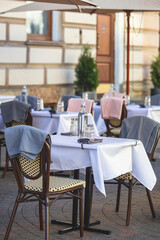 Fototapeta na wymiar View of empty street cafe restaurant outdoor terrace veranda decoration on pedestrian european street, with chairs, tables decorated with white tablecoth, pink and grey blanket, bottles of water