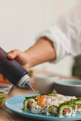 Close upmale hand with bottle adds sauce to sushi plate. Food delivery concept