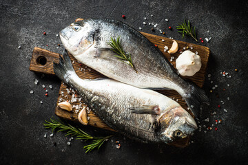 Fresh fish dorado on black stone table with ingredients for cooking. Top view.