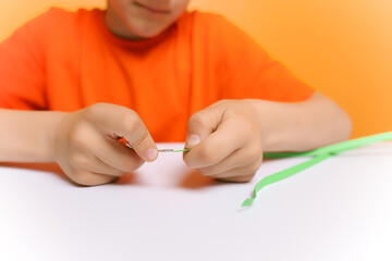 the hands of a boy in close up who inserts thin paper strips into a twisting tool in the quilling technique