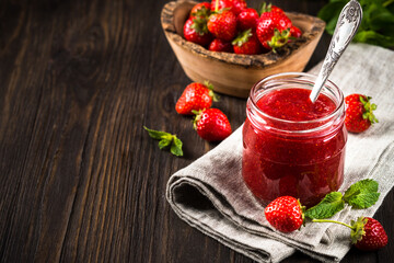 Strawberry jam in the glass jar with fresh berries at wooden table.