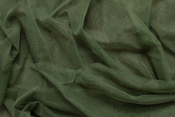 Texture of wrinkled, crumpled green tulle mesh fabric on a pink background close-up. background for...