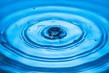 Macro view of drops making circles on blue water surface isolated on background.