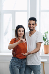 Excited African American young family show keys to own home, happy mixed race couple praise buying first house together, smiling husband and wife purchase new property. Ownership concept