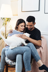 Lovely mixed-races young happy joyful couple male and female smiling in good mood resting at home in living room with pet animal holding cat in hands, pet lover concept