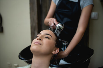 Fototapeta premium Hairdresser washing hair of a beautiful young adult woman in hair salon.